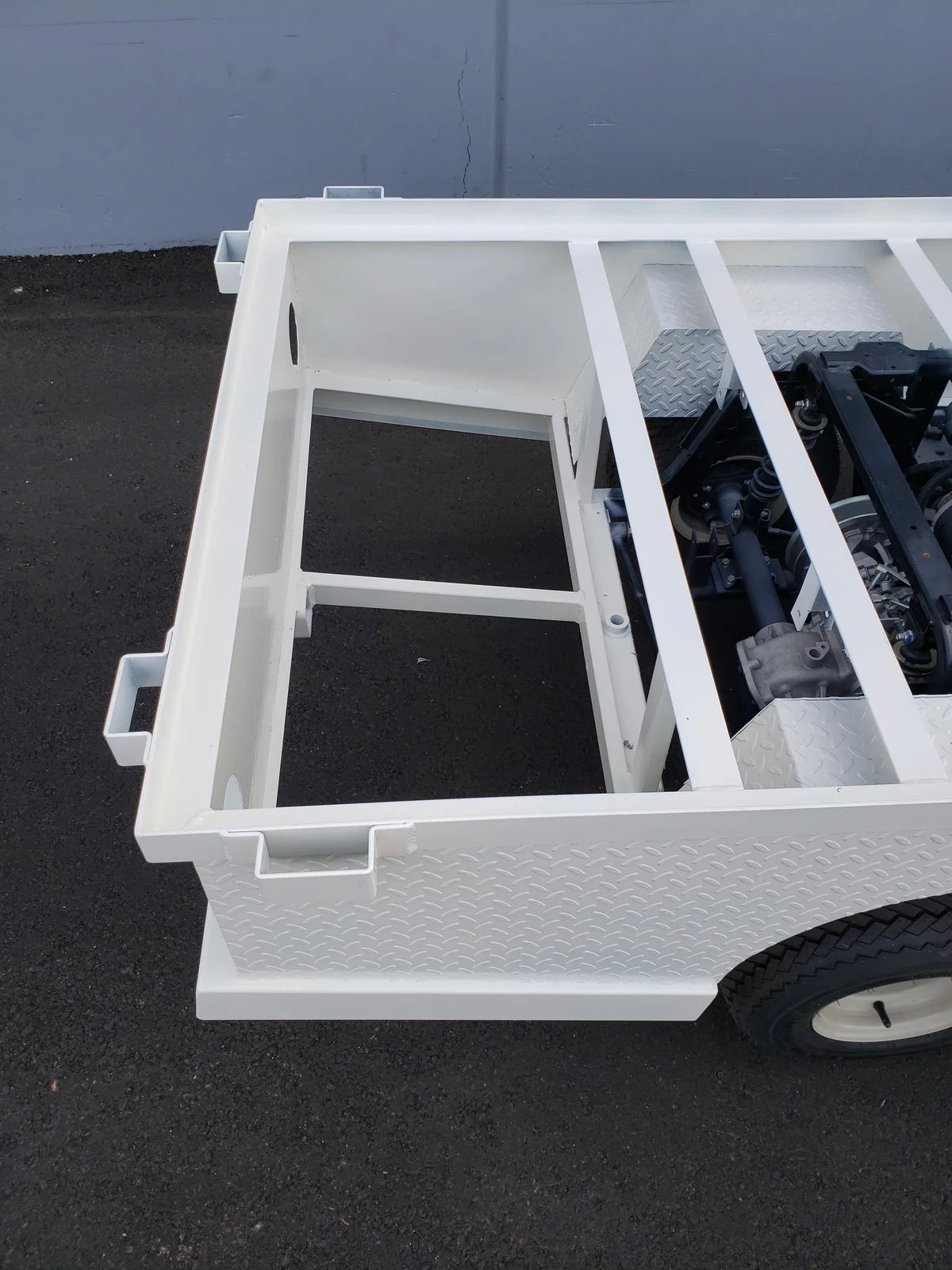 Close-up of a white metal frame structure with diamond plate paneling designed as STAKEBED POCKETS FOR 6 FT FLATBED DECK CONVERSION, custom fabrication for golf carts.
