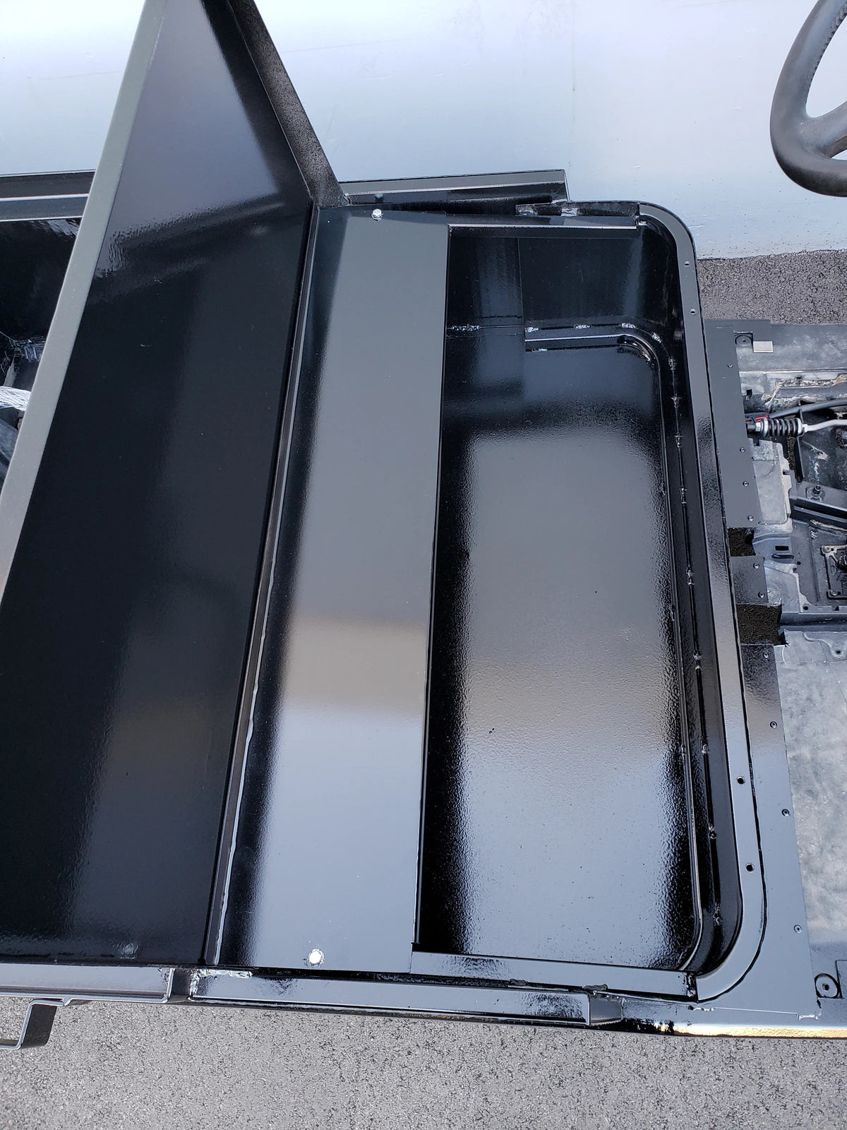 Black metal flatbed cargo area with hinged cover open, showing smooth interior surface designed for custom fabrication, part of the EZGO-RXV-ST-FLAT-72 EZ GO RXV FLATBED RETROFIT CONVERSION.