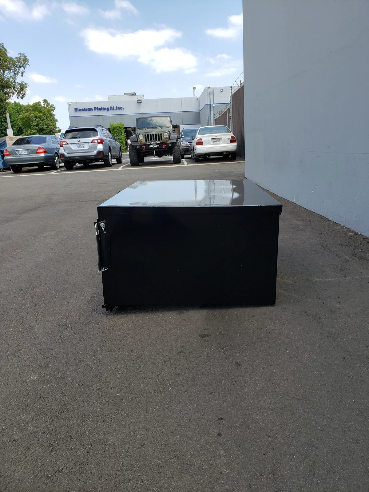 Black heavy-duty rectangular cargo box with locking mechanism designed for custom fabrication on golf carts, shown outdoors on pavement near parked vehicles, CUSH-HP-CARGO31 CUSHMAN HAULER PRO HEAVY-DUTY LOCKING CARGO BOX.