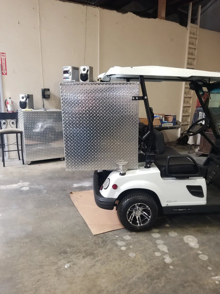 White golf cart equipped with a custom fabrication shiny metal utility box mounted on the rear, showcasing the TOM-35X32X37-RB Tomberlin Emerge Rear Box designed for cargo and specialty golf cart use.