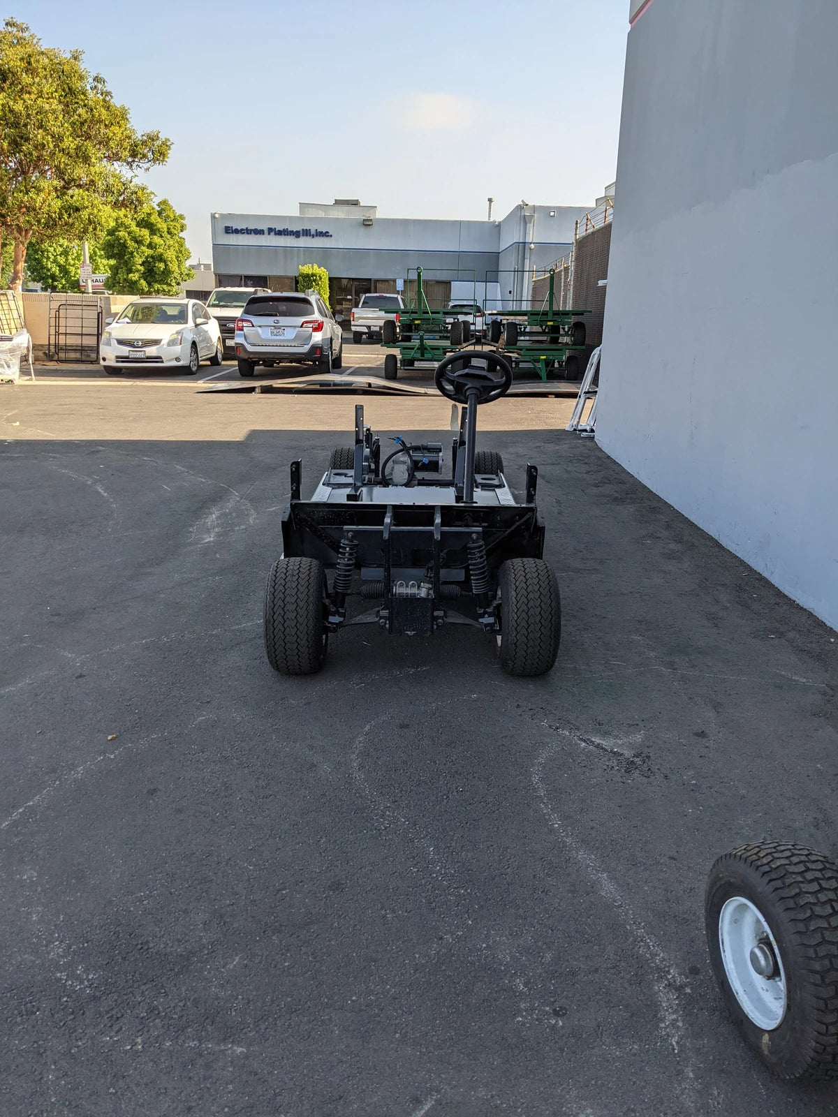 Front view of a custom fabrication golf cart chassis with steering wheel installed in an industrial outdoor area, showing the EZGO-RXV-PS6-4F+2B EZGO RXV 6 PASSENGER CONVERSION.