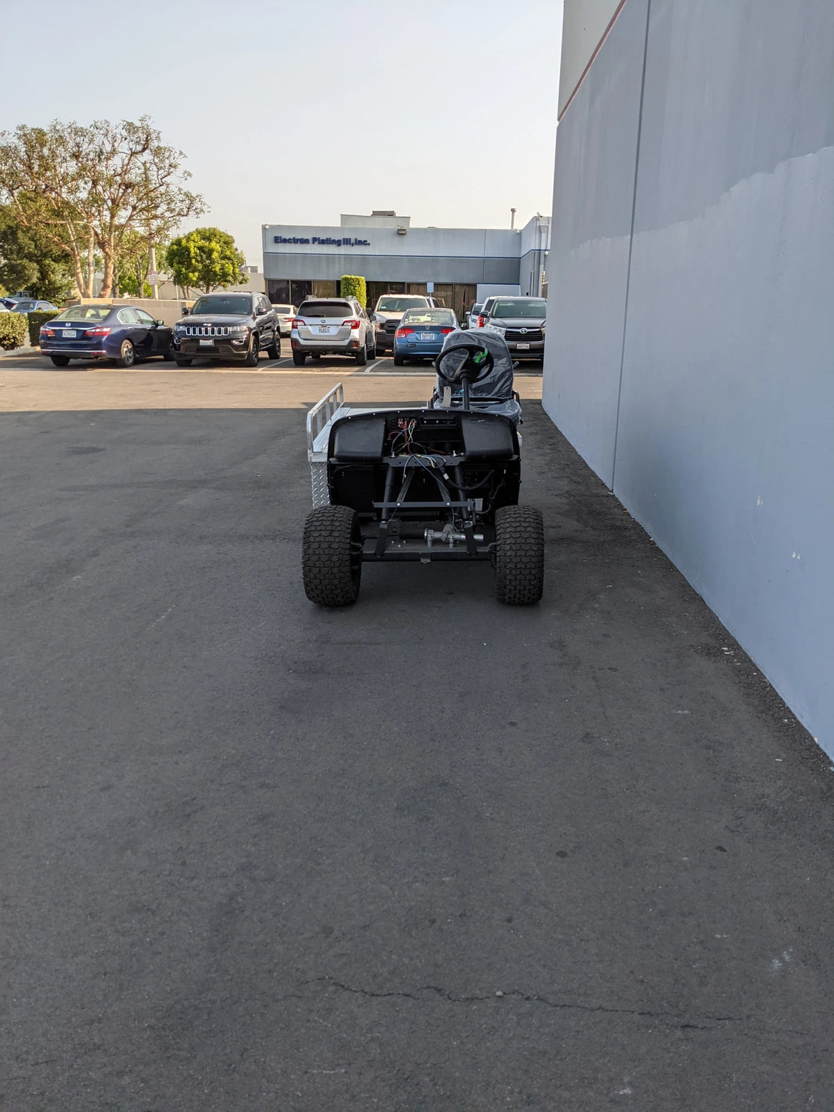 Rear view of a custom fabrication showing the EZGO-EMT-84X24 EMT GOLF CART BED CONVERSION FOR EZ GO TXT GOLF CART in an outdoor parking area with other vehicles in the background.