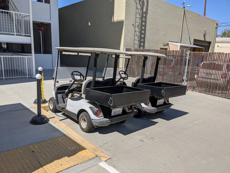 Two golf carts parked side by side, both equipped with YAM-DRIVE-UTIL31 YAMAHA DRIVE HEAVY-DUTY INDUSTRIAL UTILITY BOX WITH TAILGATE; custom fabrication for golf carts.