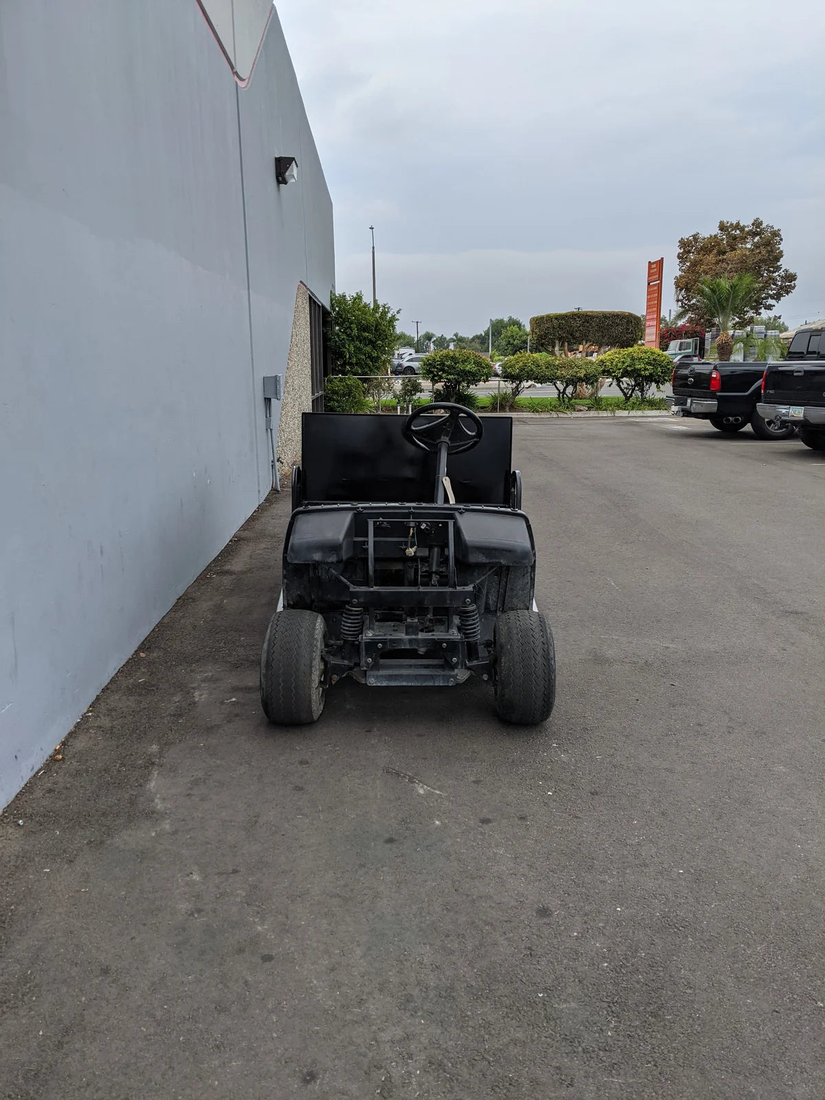 Front view of a custom-fabricated black golf cart modified with the YAM-UMAX-ST-FLAT-72 Yamaha Umax 6 foot Flatbed Conversion, parked beside a building outdoors.