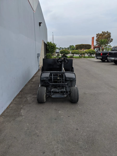 Front view of a custom-fabricated black golf cart modified with the YAM-UMAX-ST-FLAT-72 Yamaha Umax 6 foot Flatbed Conversion, parked beside a building outdoors.