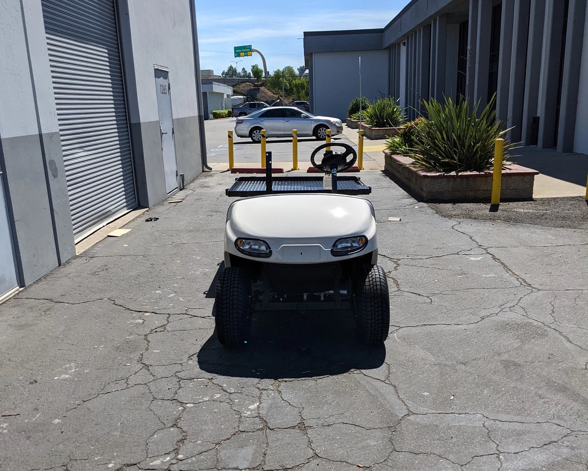 EZGO-TXTVAL-DECK48X48 EZ GO TXT, VALOR, AND MEDALIST DIAMOND PLATE STEEL UTILITY DECK 48″ X 48″ WITH STAKE POCKETS mounted on a golf cart parked outside a commercial building, custom fabrication for golf carts.