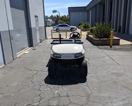 EZGO-TXTVAL-DECK48X48 EZ GO TXT, VALOR, AND MEDALIST DIAMOND PLATE STEEL UTILITY DECK 48″ X 48″ WITH STAKE POCKETS mounted on a golf cart parked outside a commercial building, custom fabrication for golf carts.