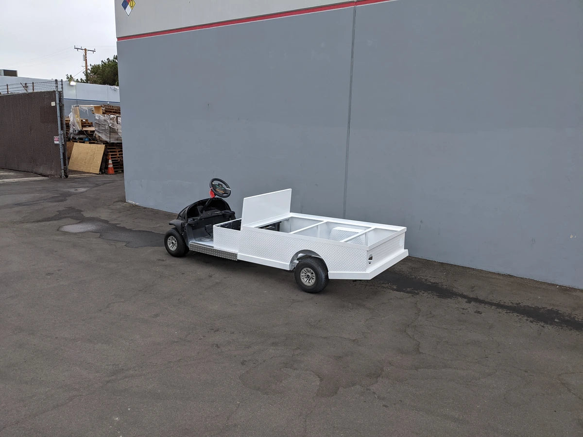 Black golf cart with a white custom flatbed cargo area parked outside near a gray wall, showcasing the CC-PREC-ST-FLAT-72 CLUB CAR PRECEDENT 6 FOOT FLATBED CONVERSION for specialized golf cart use.
