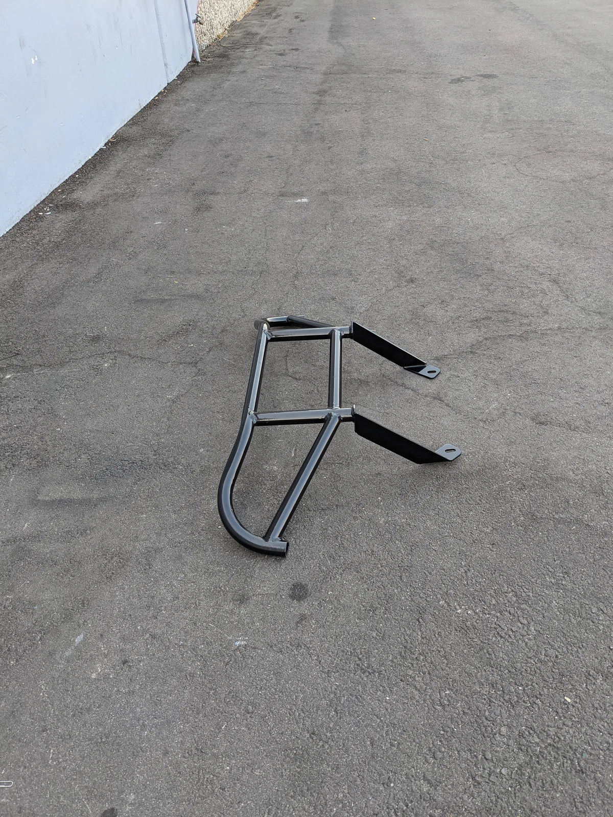 Black metal TOM-EMERGE-E2-BG TOMBERLIN EMERGE E2 BRUSH GUARD designed as custom fabrication for golf carts, shown on asphalt surface.