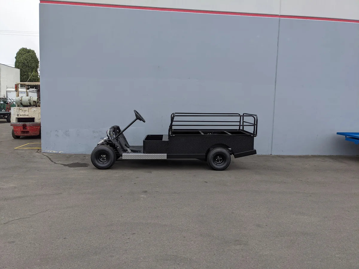 Black custom flatbed golf cart conversion with drop rails parked outdoors against a gray wall, showcasing the YAM-DRIVE2-ST-FLAT-72 YAMAHA DRIVE 2 6FT FLATBED CONVERSION for utility and cargo use.