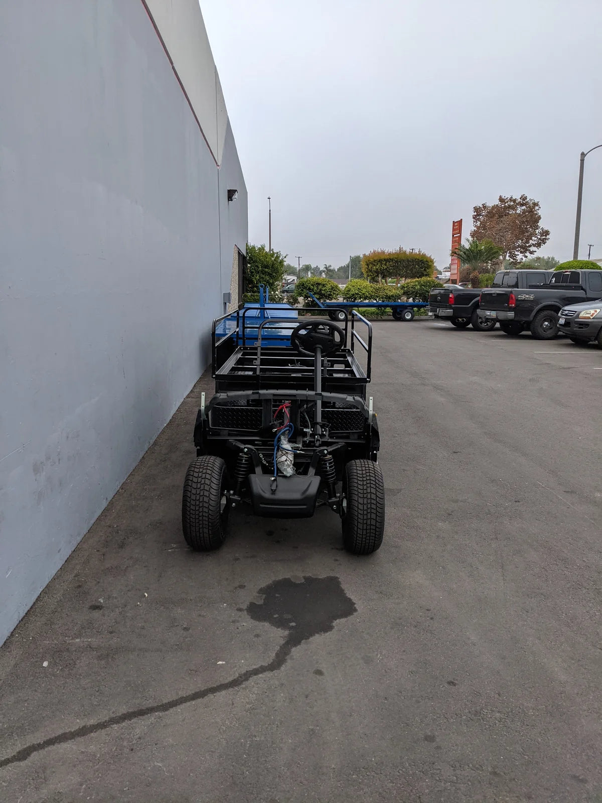 Front view of YAM-DRIVE2-ST-FLAT-72 YAMAHA DRIVE 2 6FT FLATBED CONVERSION golf cart with black frame and flatbed, showcasing custom fabrication for golf carts in an outdoor parking area.