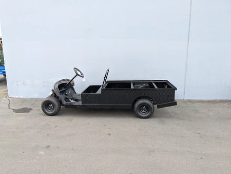 Side view of a partially assembled custom flatbed golf cart conversion with open cargo area and black diamond plate surface, designed as YAM-DRIVE2-ST-FLAT-72 YAMAHA DRIVE 2 6FT FLATBED CONVERSION for unique golf cart utility needs.