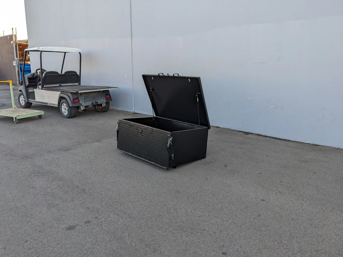Black heavy duty locking cargo box with open lid designed for golf carts, shown beside a golf cart, custom fabrication for golf carts, CUSH-800-CARGO31-GS HEAVY DUTY LOCKING CARGO BOX FOR CUSHMAN 800 SERIES