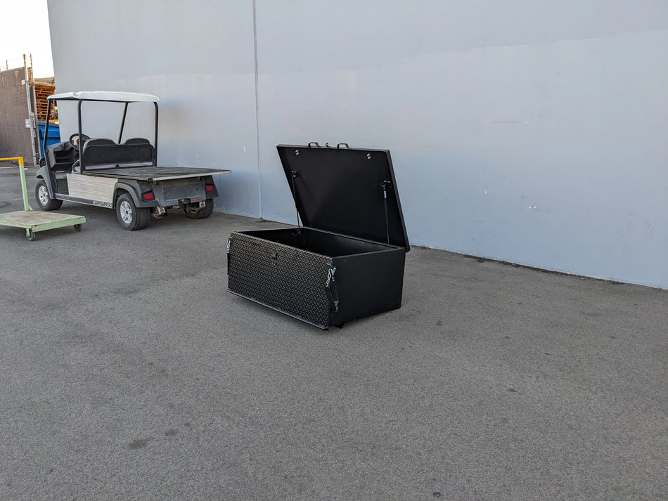 Black heavy duty locking cargo box with open lid designed for golf carts, shown beside a golf cart, custom fabrication for golf carts, CUSH-800-CARGO31-GS HEAVY DUTY LOCKING CARGO BOX FOR CUSHMAN 800 SERIES