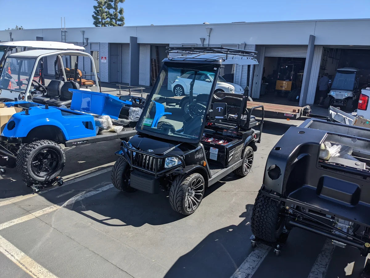 Black golf cart equipped with TOM-EMERGE2PASS-49RR3 Tomberlin Emerge 2 Passenger Roof Rack parked outdoors among other custom golf carts, showcasing unique value: custom fabrication for golf carts.
