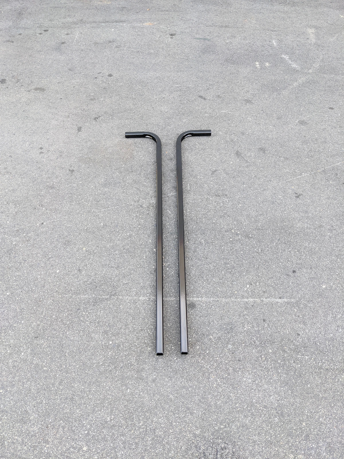 Two black metal bars with right-angle bends laid on a concrete surface, designed as CART-RTS GENERIC GOLF CART REAR TOP SUPPORT for golf cart accessories.