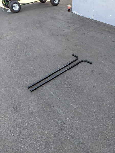 Two black metal rods lying on asphalt near a golf cart, designed as the CART-RTS GENERIC GOLF CART REAR TOP SUPPORT for reinforcing golf cart tops.