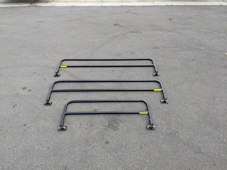 Three black metal rails laid out on asphalt surface showcasing DROP RAILS 48″ X 66″ X 18″ FOR 5-1/2 FT FLATBED CONVERSION designed for custom fabrication for golf carts.