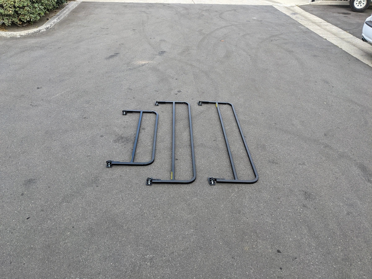 Three black metal drop rails laid out on pavement, designed as DROP RAILS 48″ X 66″ X 18″ FOR 5-1/2 FT FLATBED CONVERSION, custom fabrication for golf carts.