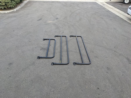 Three black metal drop rails laid out on pavement, designed as DROP RAILS 48″ X 66″ X 18″ FOR 5-1/2 FT FLATBED CONVERSION, custom fabrication for golf carts.