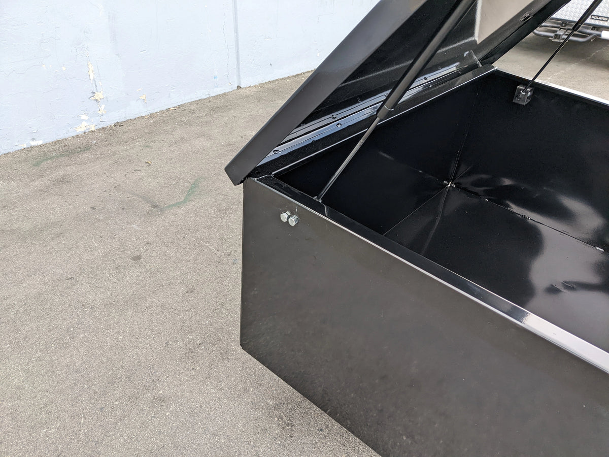 Black metal utility box lid held open by CARGO31-GAS-SPRING-RETROFIT GAS SPRING KIT FOR CART HAULERS CARGO BOX LID OPENING AND CLOSING, showing interior and mounting hardware.