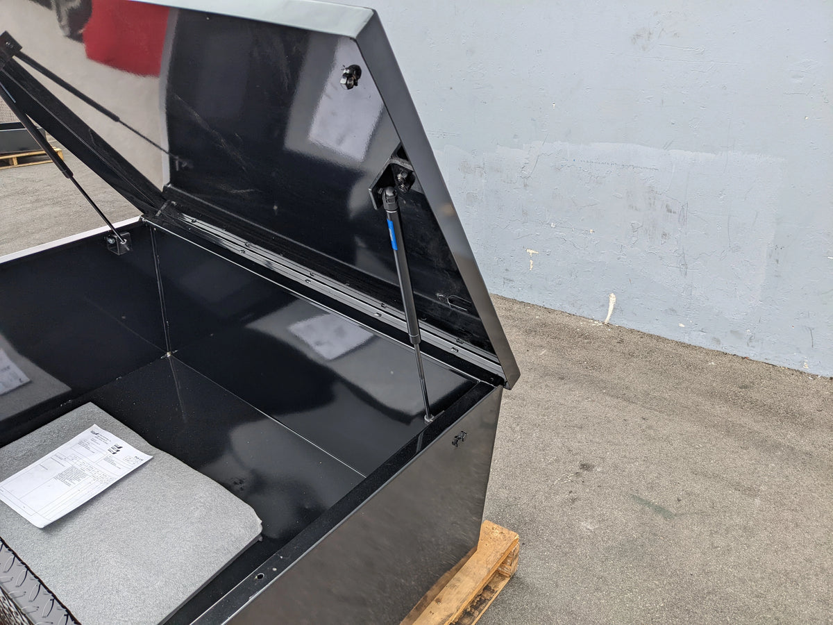 Close-up of a black utility box lid held open by a gas spring showing installation details of the CARGO31-GAS-SPRING-RETROFIT GAS SPRING KIT FOR CART HAULERS CARGO BOX LID OPENING AND CLOSING.
