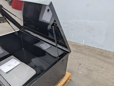 Close-up of a black utility box lid held open by a gas spring showing installation details of the CARGO31-GAS-SPRING-RETROFIT GAS SPRING KIT FOR CART HAULERS CARGO BOX LID OPENING AND CLOSING.
