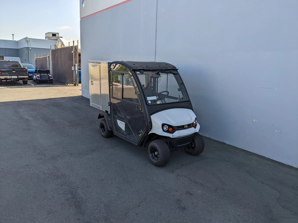 Small black and white utility vehicle with enclosed cab and large metal cargo box with locking doors, designed as CUSH-HP-CARGO42X48X42-4D CUSHMAN HAULER PRO WITH CAB CARGO BOX WITH LOCKING DOORS, custom fabrication for golf carts.