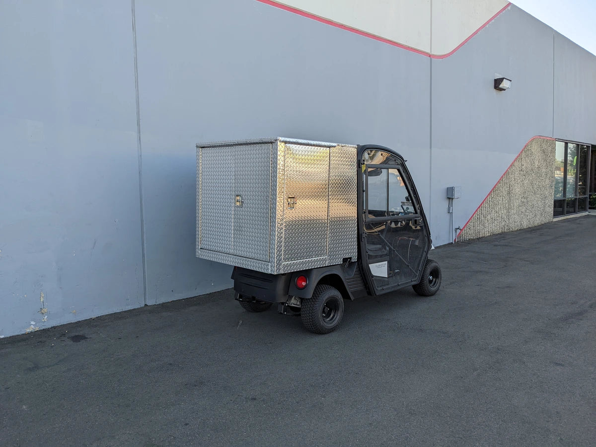 CUSH-HP-CARGO42X48X42-4D CUSHMAN HAULER PRO WITH CAB CARGO BOX WITH LOCKING DOORS mounted on a utility vehicle parked outside a commercial building, featuring custom fabrication for golf carts.