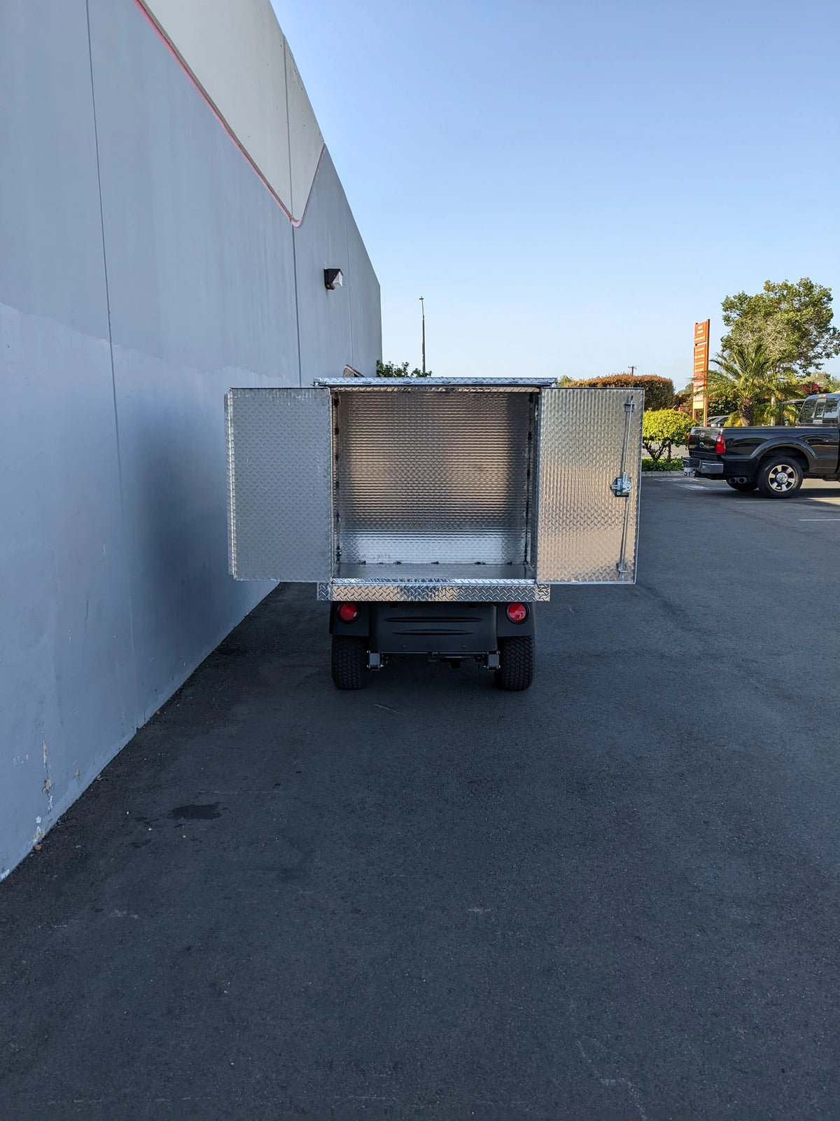 Rear view of CUSH-HP-CARGO42X48X42-4D CUSHMAN HAULER PRO WITH CAB CARGO BOX WITH LOCKING DOORS showing open diamond plate metal cargo box, custom fabrication for golf carts.