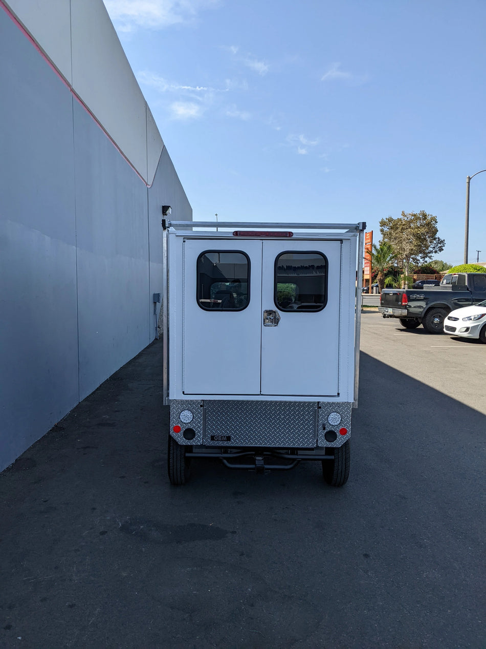 Rear view of a small utility vehicle equipped with the FMB-GEM-52X70X48-SL-D3W3 FLATBED ALUMINUM SMOOTH MULTI-PURPOSE LIGHT BOX FOR GEM ELXD 52″ WIDE X 70″ LONG X 48″ TALL WITH LOCKING DOORS, custom fabrication for golf carts.