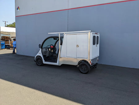 Small utility golf cart fitted with FMB-GEM-52X70X48-SL-D3W3 FLATBED ALUMINUM SMOOTH MULTI-PURPOSE LIGHT BOX FOR GEM ELXD 52″ WIDE X 70″ LONG X 48″ TALL WITH LOCKING DOORS, custom fabricated for golf carts.