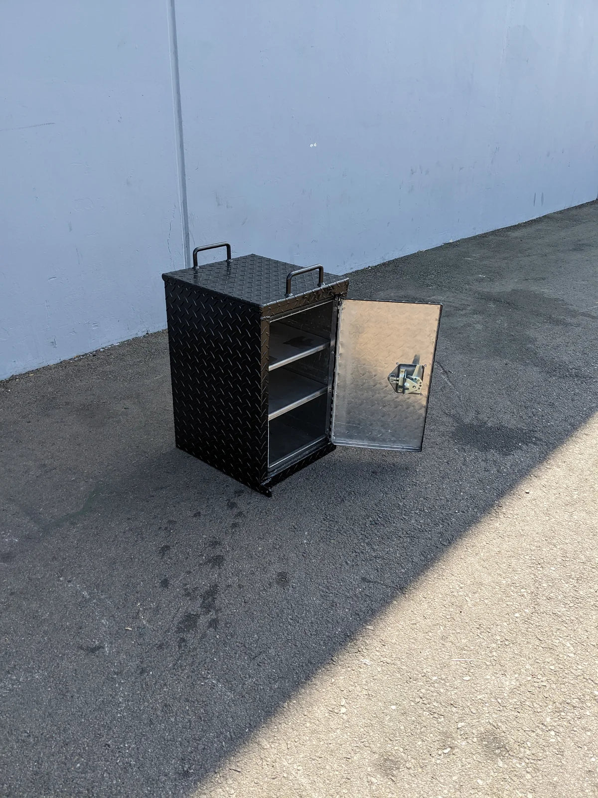 TB-15.5X16X20 LOCKING STORAGE BOX with handles shown open on a paved surface, featuring a durable textured metal exterior and internal shelving, custom fabricated for golf carts.