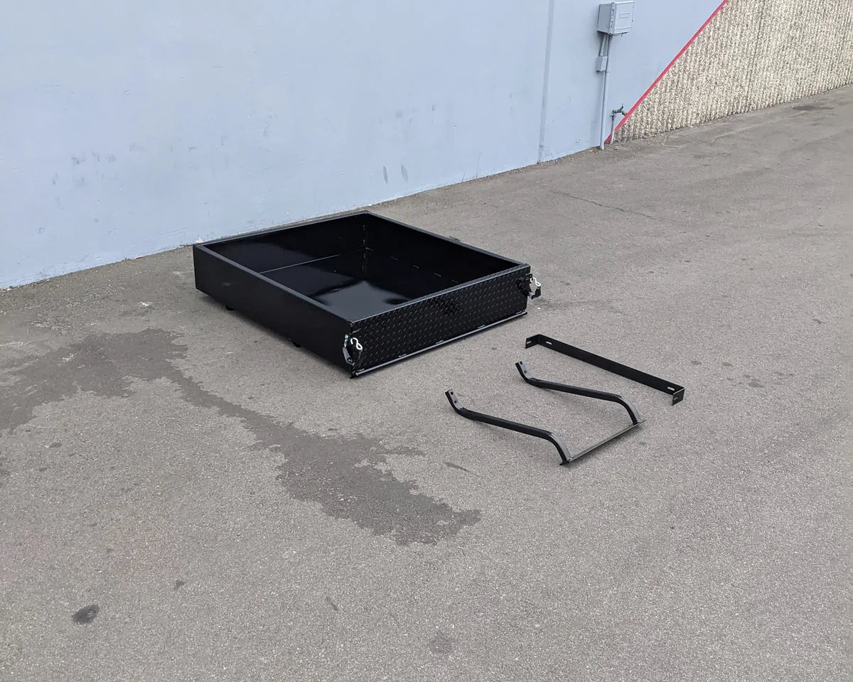 TOM-E2-UTIL48 TOMBERLIN EMERGE 2 Utility Box 48″ long black metal cargo box with custom fabrication for golf carts shown with mounting brackets on concrete surface.