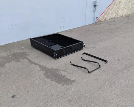TOM-E2-UTIL48 TOMBERLIN EMERGE 2 Utility Box 48″ long black metal cargo box with custom fabrication for golf carts shown with mounting brackets on concrete surface.