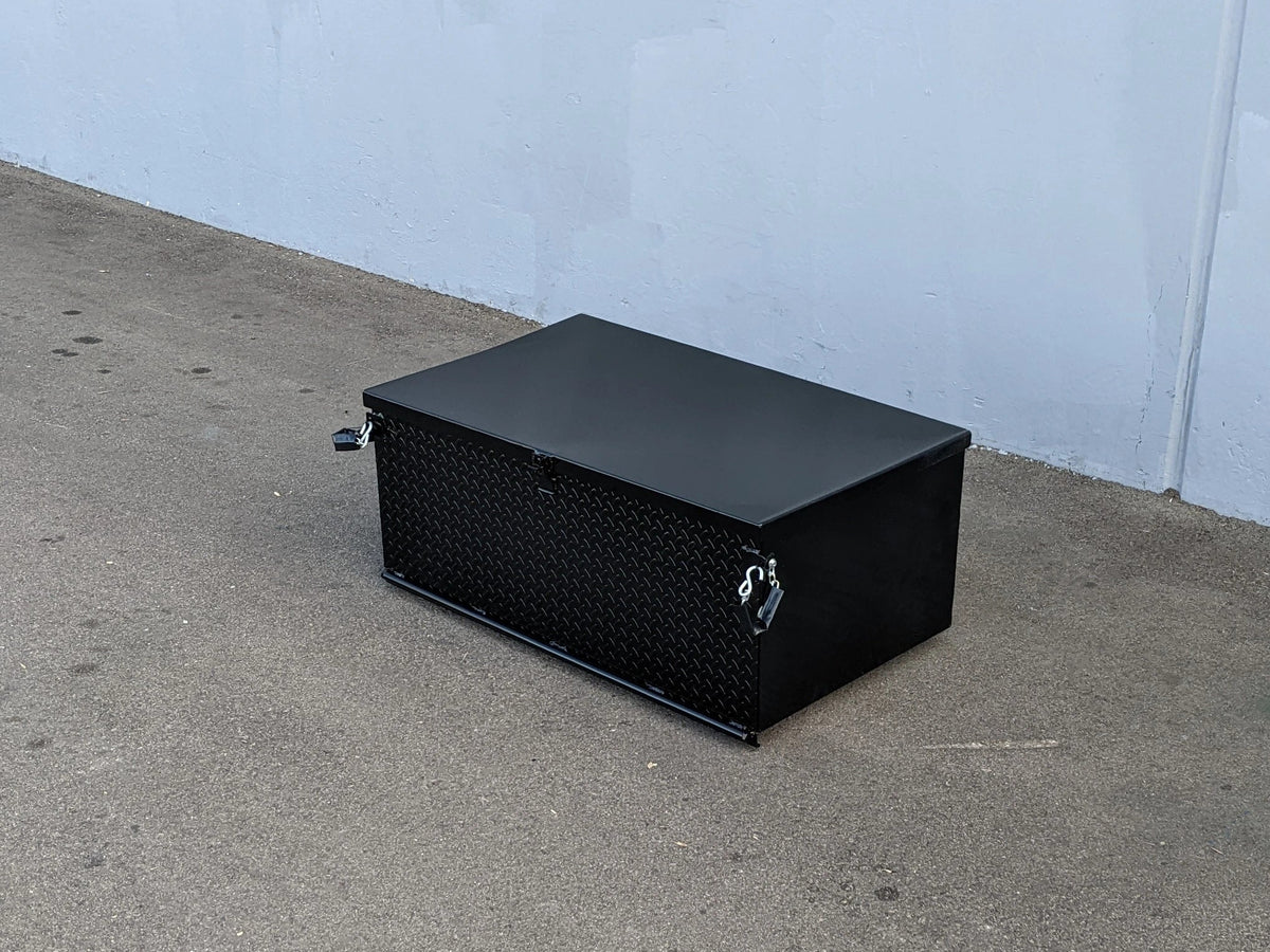 Black rectangular toolbox on a concrete floor against a light blue wall.