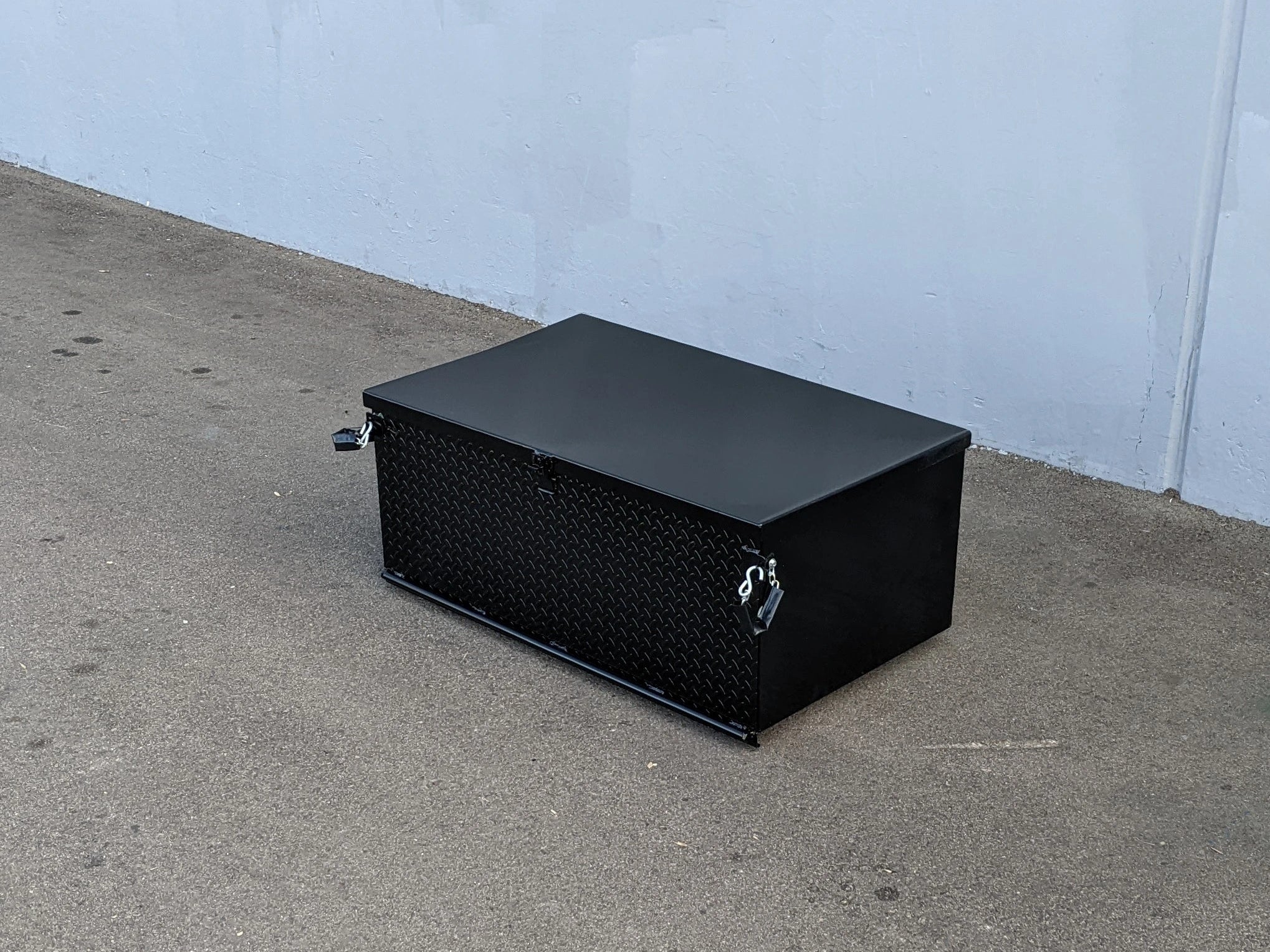 Black rectangular toolbox on a concrete floor against a light blue wall.