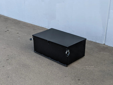 Black rectangular toolbox on a concrete floor against a light blue wall.