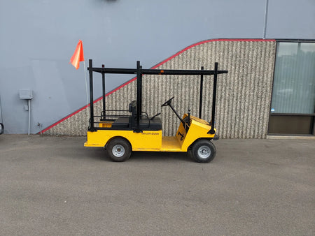 Yellow golf cart equipped with a black metal TD-R380-44X96-TLR DECK top ladder rack with deck, designed for custom fabrication for golf carts, parked outdoors near a building wall.