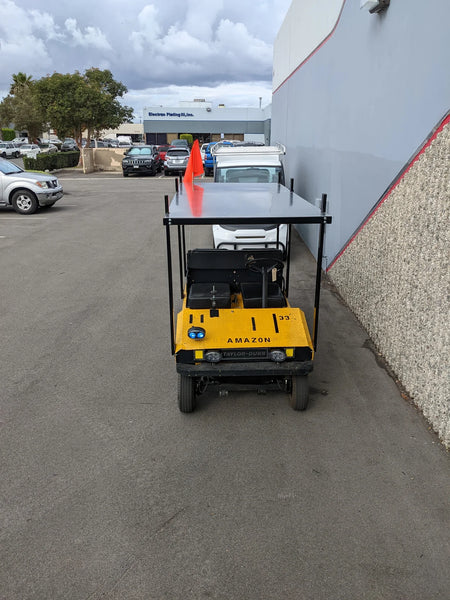 Yellow utility golf cart fitted with the TD-R380-44X96-TLR DECK top ladder rack with deck, parked by a warehouse wall, showcasing custom fabrication for golf carts.
