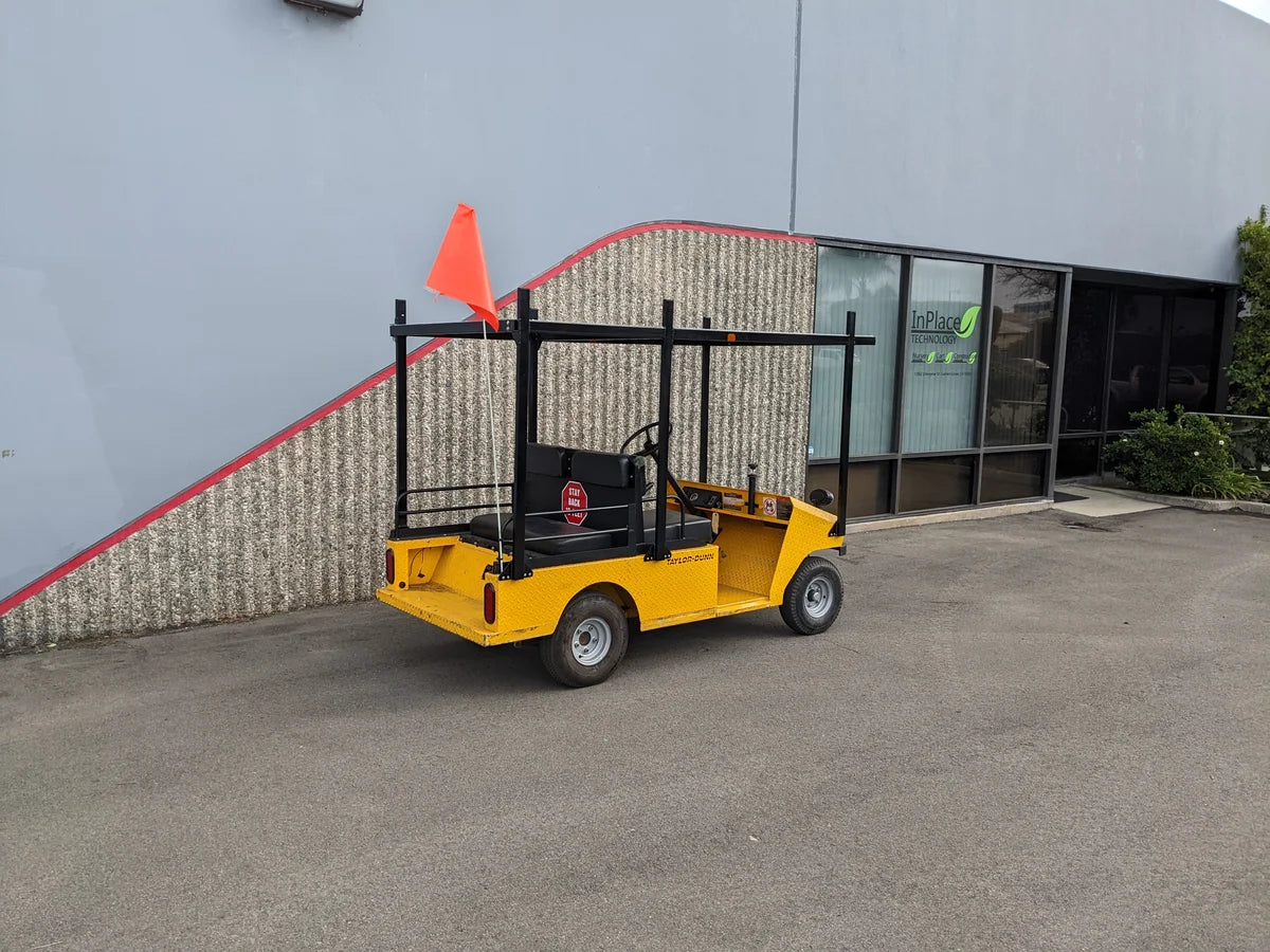 Yellow golf cart equipped with a TD-R380-44X96-TLR DECK top ladder rack with deck, custom fabricated for golf carts, parked outside commercial building.