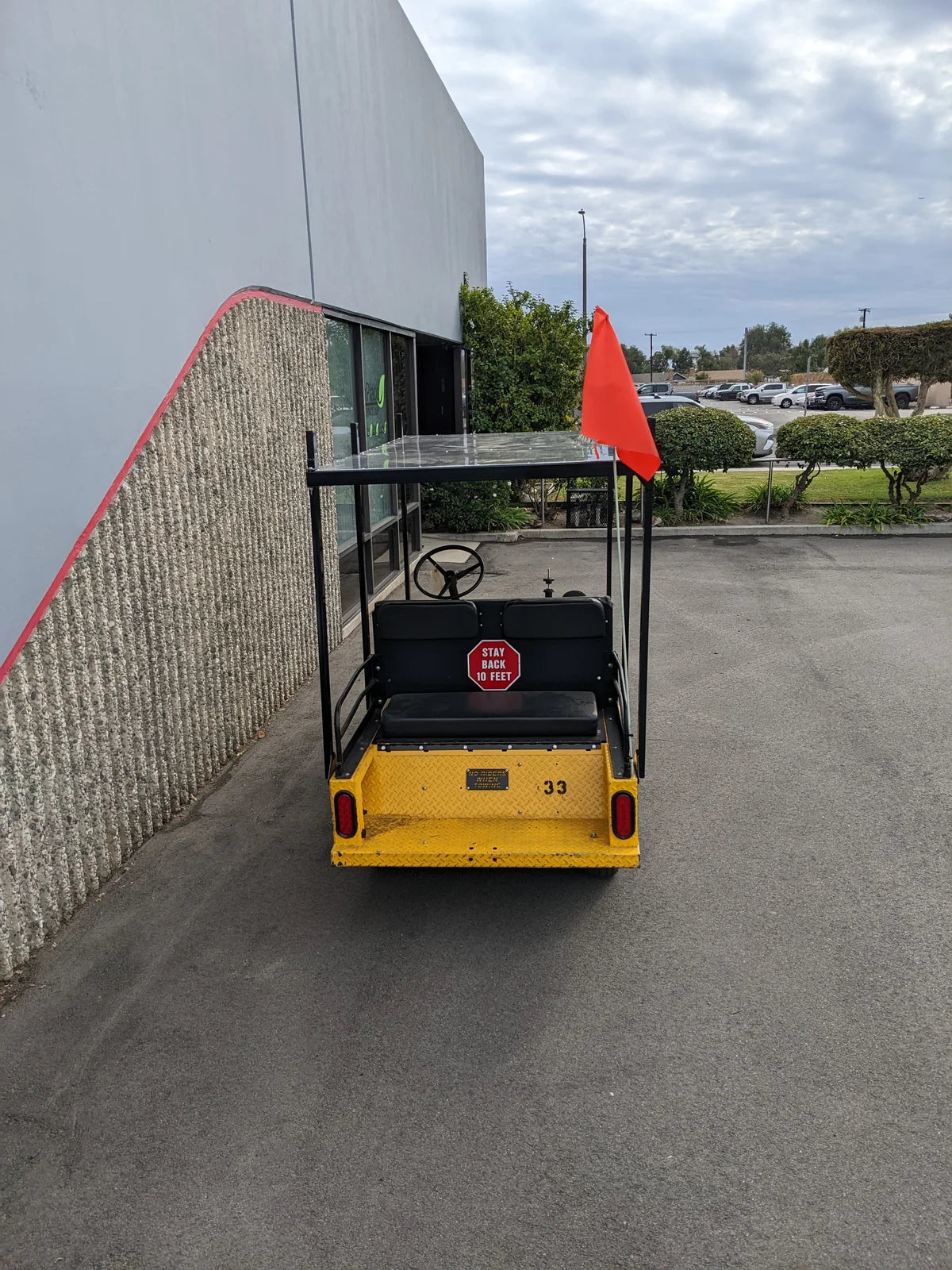 Rear view of a yellow golf cart featuring a TD-R380-44X96-TLR DECK top ladder rack with deck, equipped with a custom fabrication for golf carts and a visible safety flag.