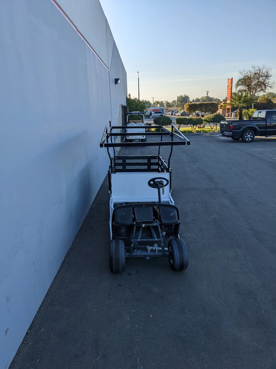 White golf cart equipped with a black FB-45X120-TLRI-INSIDE MOUNT 10 FT Top Mount Ladder Rack for Flatbed, parked outside near a building, custom fabrication for golf carts.