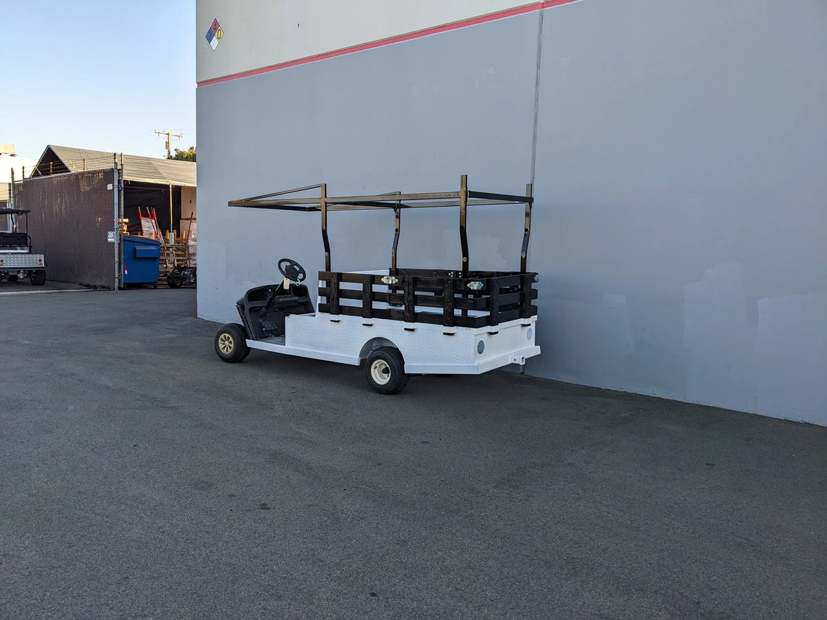 White golf cart equipped with a custom fabrication FB-45X120-TLRI-INSIDE MOUNT 10 FT Top Mount Ladder Rack for Flatbed, parked outside near a building wall.