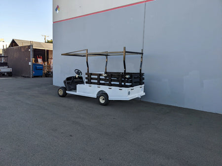White golf cart equipped with a custom fabrication FB-45X120-TLRI-INSIDE MOUNT 10 FT Top Mount Ladder Rack for Flatbed, parked outside near a building wall.