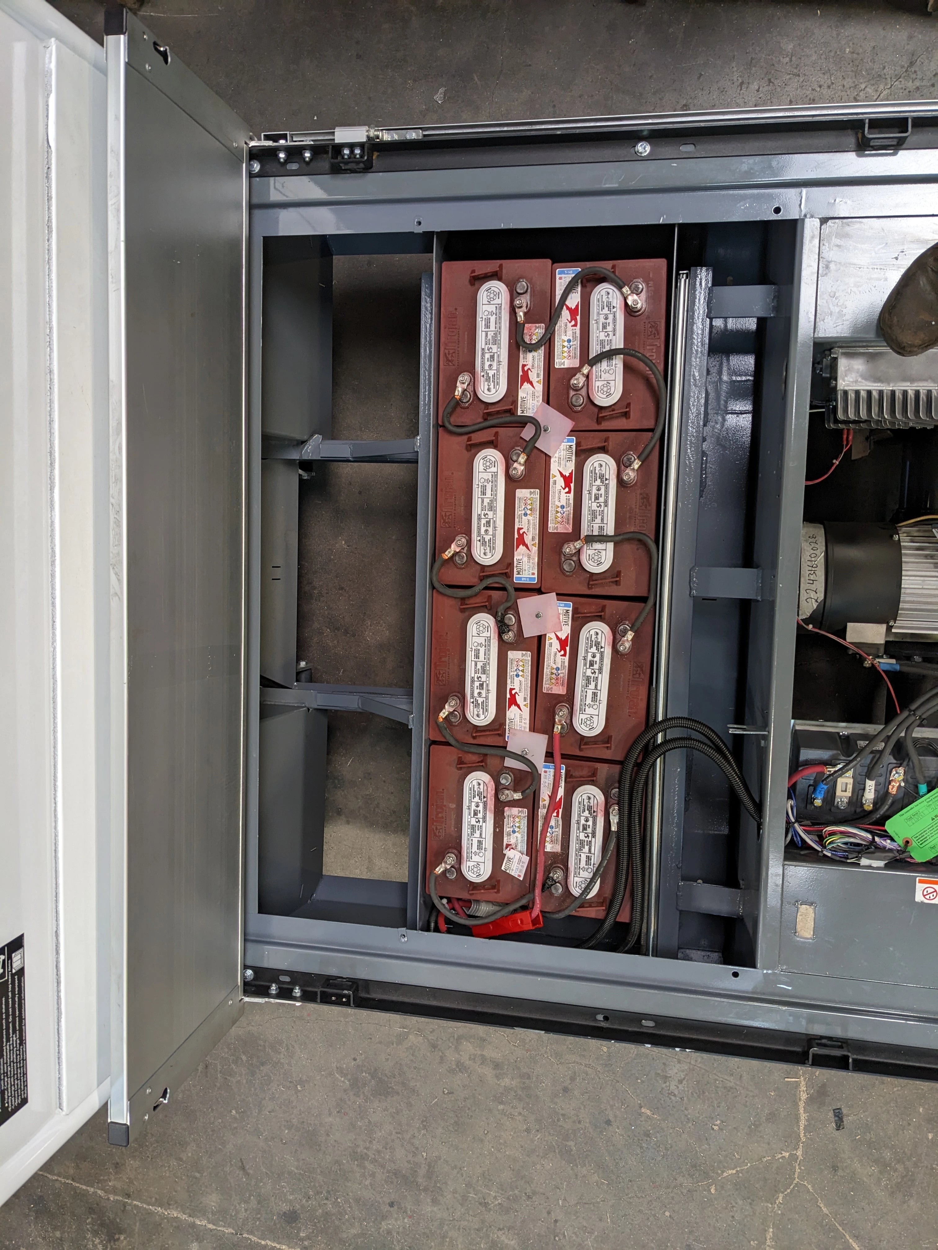 BIGFOOT XL BATTERY SLIDE-OUT RETROFIT FOR TAYLOR-DUNN BIGFOOT XL showing an open compartment with multiple connected batteries and visible wiring inside a metal frame.