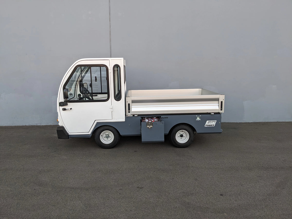 Side view of a compact utility vehicle equipped with BIGFOOT XL BATTERY SLIDE-OUT RETROFIT FOR TAYLOR-DUNN BIGFOOT XL, featuring a flatbed cargo area and enclosed cabin.