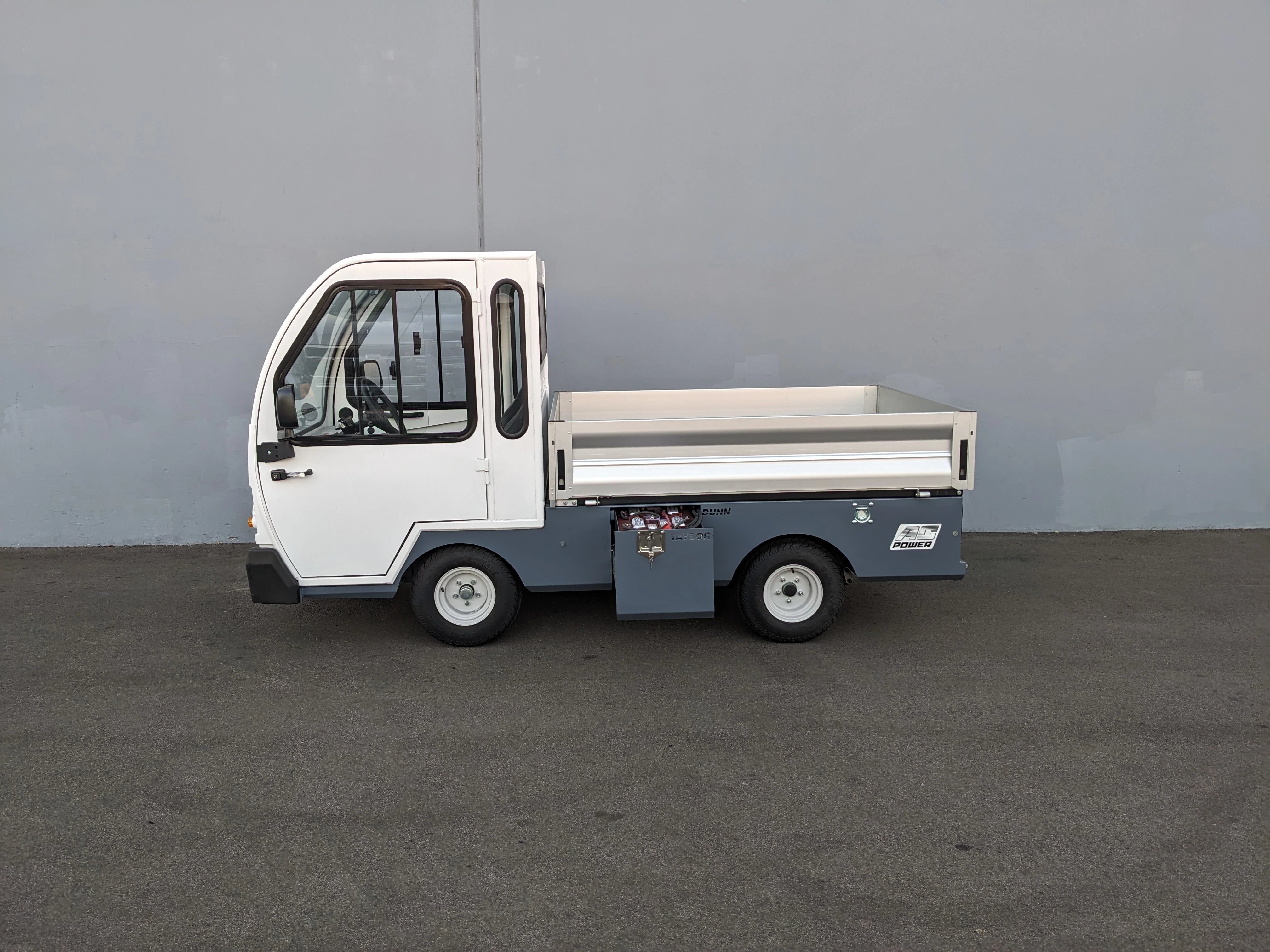 Side view of a compact utility vehicle equipped with BIGFOOT XL BATTERY SLIDE-OUT RETROFIT FOR TAYLOR-DUNN BIGFOOT XL, featuring a flatbed cargo area and enclosed cabin.