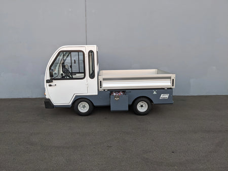 Side view of a compact utility vehicle equipped with BIGFOOT XL BATTERY SLIDE-OUT RETROFIT FOR TAYLOR-DUNN BIGFOOT XL, featuring a flatbed cargo area and enclosed cabin.
