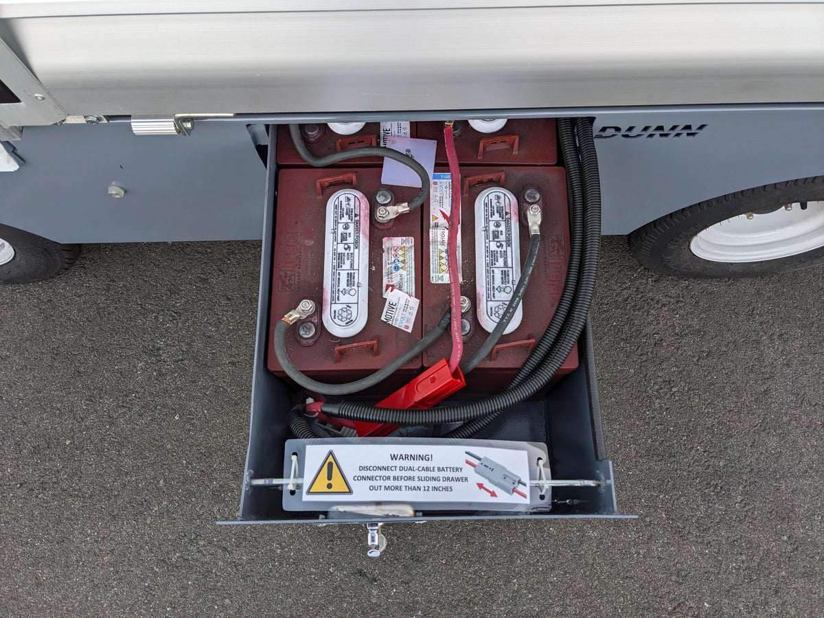 Open battery compartment showing two connected batteries with warning label inside a utility vehicle for BIGFOOT XL BATTERY SLIDE-OUT RETROFIT FOR TAYLOR-DUNN BIGFOOT XL